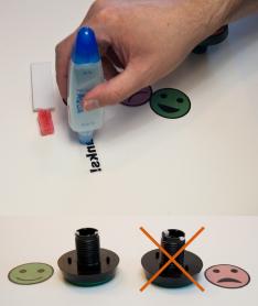 Top: Hand applying glue to the back of stickers. Bottom: Two buttons and two stickers. The left button is paired with a green smiling face sticker aligned parallel to the guide pegs on the underside of the button. The right button has an 'X' through it, showing that the frowning sticker was not properly aligned with the guide pegs.