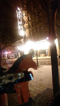 A sparkle pony pin is held up in front of the old Tampa theatre sign. It's night and the impression is that sparkle pony is thinking about going to the theatre.